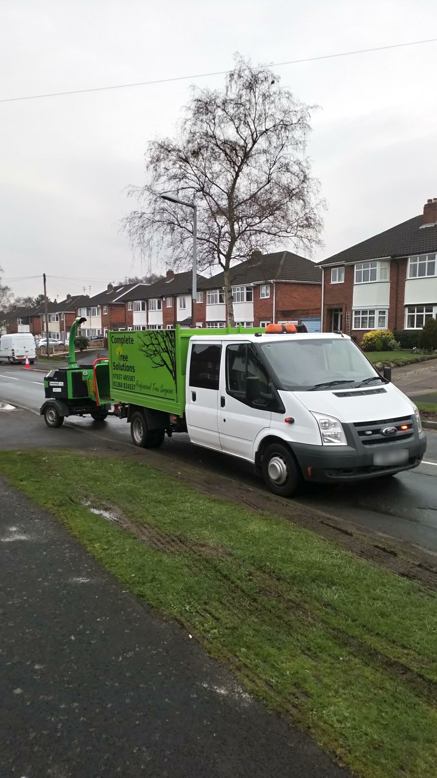 The lime green Complete Tree Solutions tipper towing a chipper